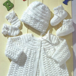 May include: A white knitted baby set including a cardigan, hat, and booties. The set is made with a textured stitch pattern and features a button closure on the cardigan.