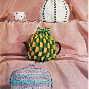 May include: Three crocheted teapot cozies in different colors and patterns. The cozies are white with green accents, yellow and green checkered, and purple and blue striped.