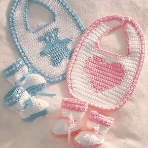 May include: Two crocheted baby bibs, one with a blue bear design and the other with a pink heart design. Two pairs of crocheted baby booties, one blue and one pink.