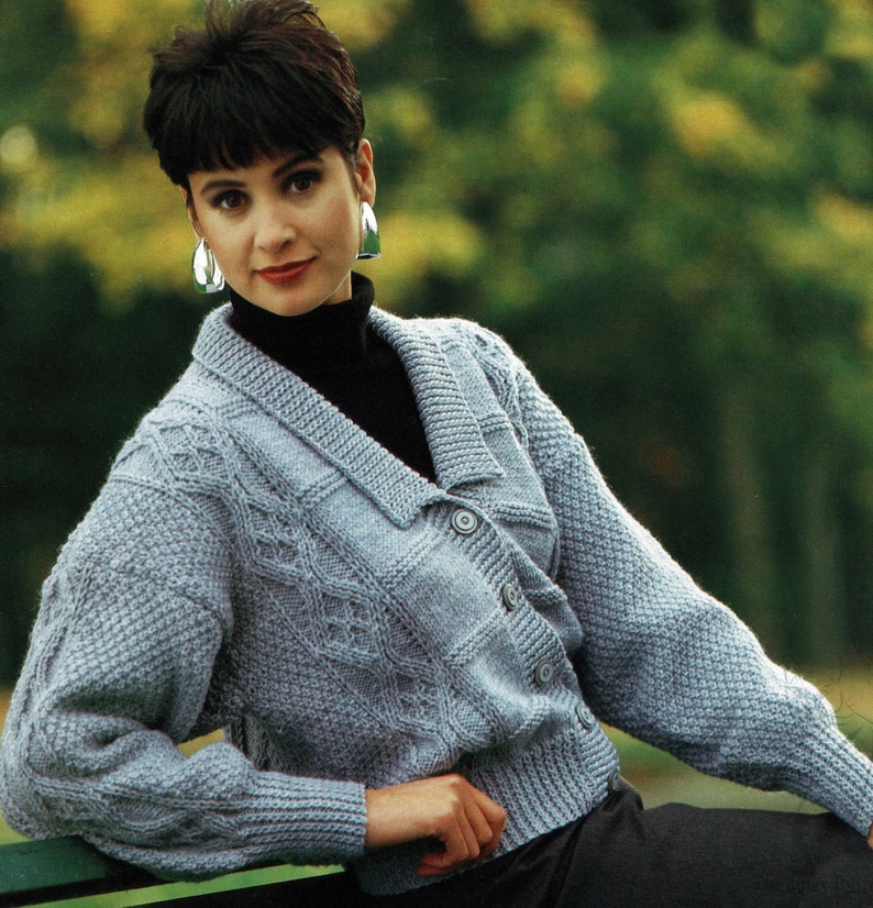 May include: A light blue knitted cardigan with a cable knit pattern and a button closure. The cardigan has a v-neck and long sleeves.