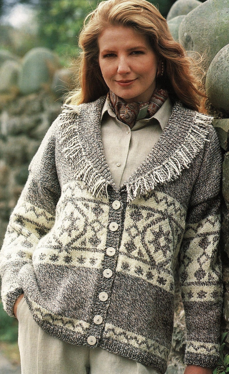 May include: A brown and white knitted cardigan with a fringe trim collar and button closure. The cardigan has a geometric pattern and is worn over a light brown shirt.