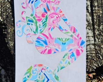 May include: A colorful mermaid sticker with a floral pattern in pink, blue, green, and orange. The mermaid is sitting with her tail curled. The sticker is on a white background.