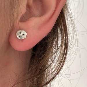 Puede incluir: Pendientes de plata con cara sonriente. Los pendientes son pequeños y delicados, y son perfectos para añadir un toque de fantasía a cualquier atuendo.