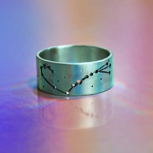 Puede incluir: Un anillo de plata con un diseño de constelación. El anillo es ancho y tiene un acabado liso y pulido.