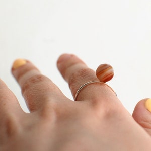 Puede incluir: Un anillo de oro con una piedra de &aacute;gata marr&oacute;n y blanca. La piedra es redonda y se encuentra en la parte superior del anillo.