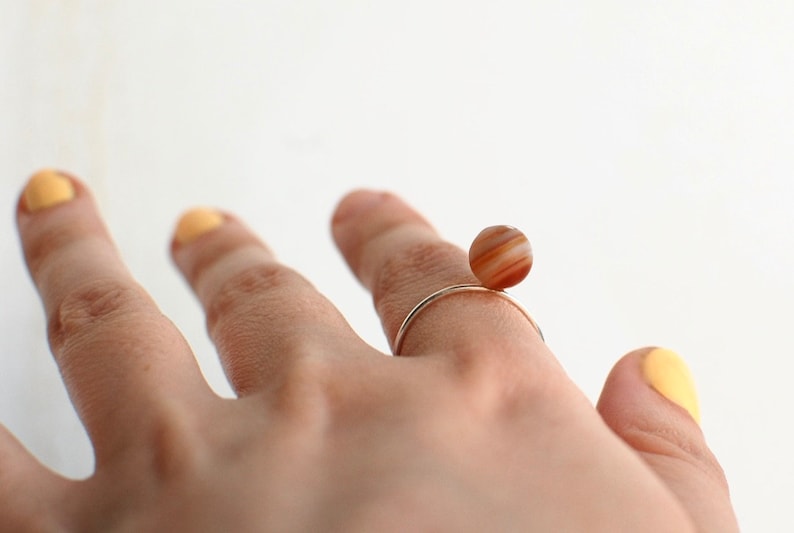 Puede incluir: Un anillo de oro con una piedra de &aacute;gata marr&oacute;n y blanca. La piedra es redonda y se encuentra en la parte superior del anillo.