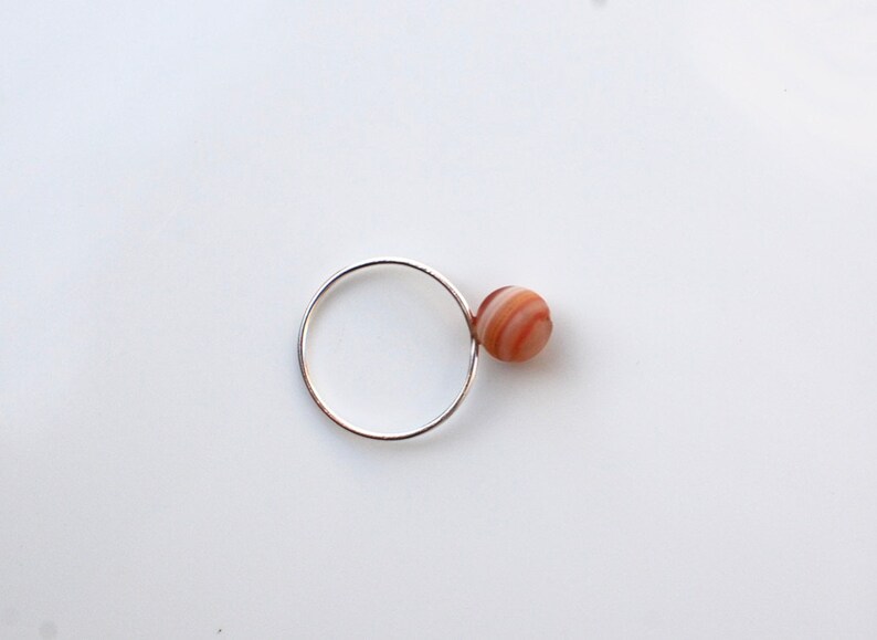 Puede incluir: Un anillo de plata con una sola piedra de &aacute;gata redonda y rayada unida al lado.
