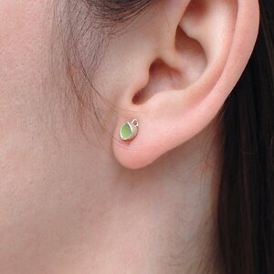 Peut inclure: Gros plan sur une oreille avec une petite boucle d'oreille verte et argent&eacute;e. La boucle d'oreille est de conception simple avec une petite pierre verte.
