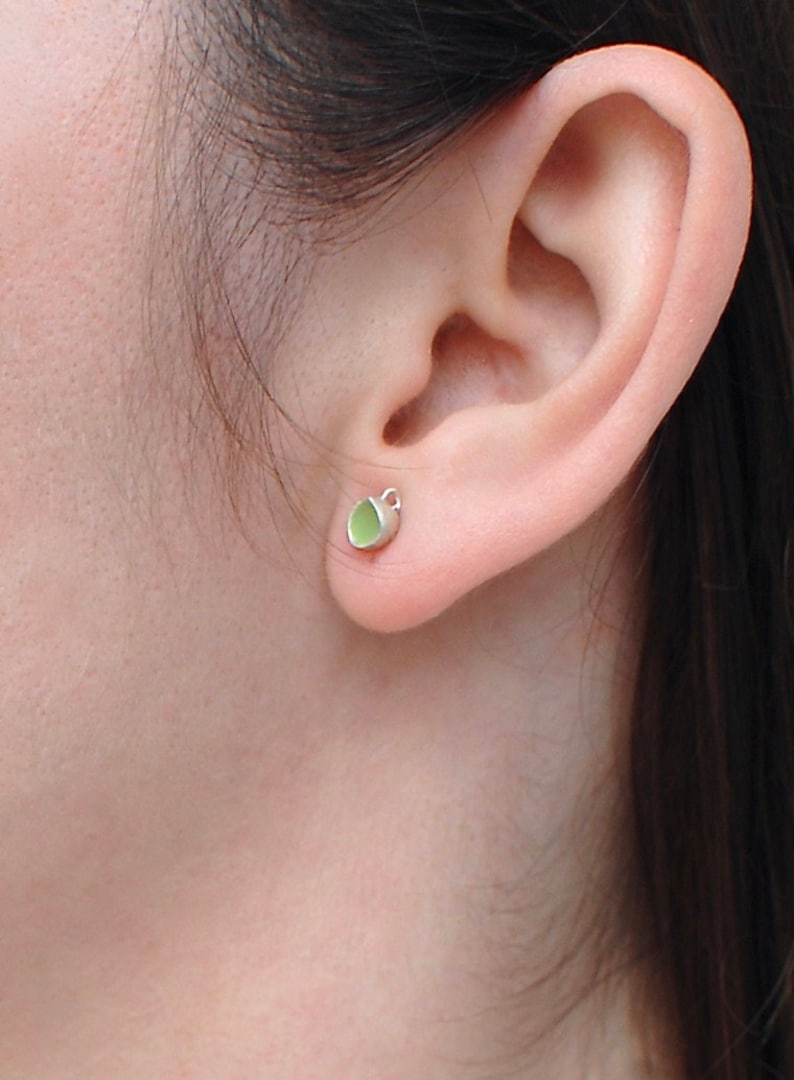 Peut inclure: Gros plan sur une oreille avec une petite boucle d'oreille verte et argent&eacute;e. La boucle d'oreille est de conception simple avec une petite pierre verte.