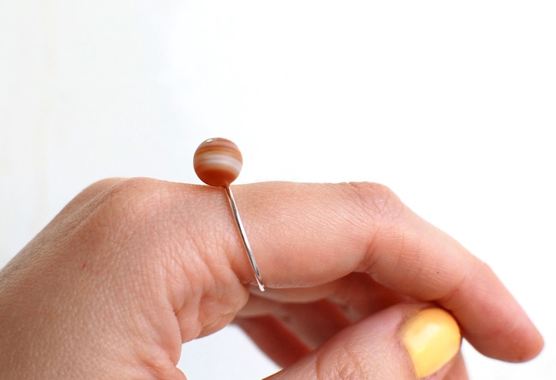 May include: A silver ring with a brown and white agate stone. The ring is on a finger.