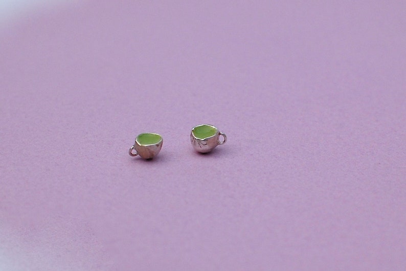 Peut inclure: Deux tasses &agrave; th&eacute; miniatures avec des poign&eacute;es argent&eacute;es et des int&eacute;rieurs en &eacute;mail vert. Les tasses sont sur un fond violet clair.