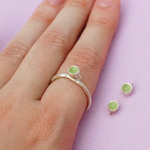 Peut inclure: Une bague en argent avec une pierre vert clair sur le dessus. Deux autres pierres vert clair sont visibles sur la table.