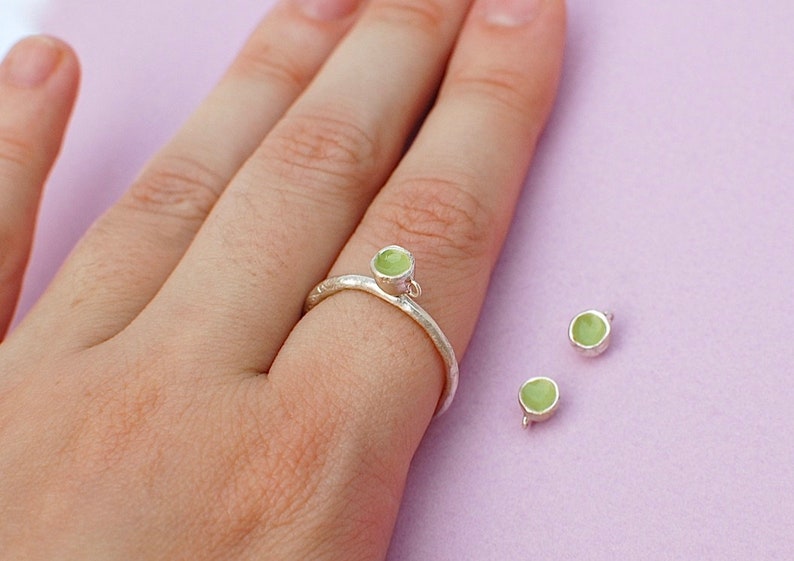 Peut inclure: Une bague en argent avec une pierre vert clair sur le dessus. Deux autres pierres vert clair sont visibles sur la table.