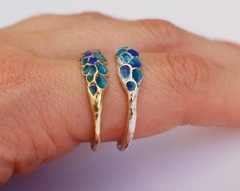 Könnte beinhalten: Zwei Ringe mit einem blauen und grünen Emaille-Design. Der Ring links ist golden und der Ring rechts ist silbern.