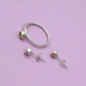 Peut inclure: Une bague en argent et une paire de boucles d'oreilles en argent avec un petit sertissage de pierre ronde vert clair. La bague est une simple bande avec une surface textur&eacute;e. Les boucles d'oreilles sont des boucles d'oreilles &agrave; tige avec un poteau et un dos papillon.