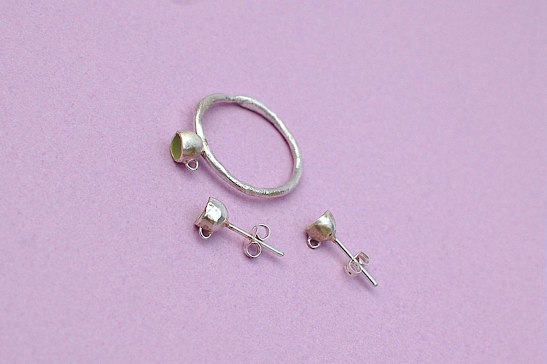 Peut inclure: Une bague en argent et une paire de boucles d'oreilles en argent avec un petit sertissage de pierre ronde vert clair. La bague est une simple bande avec une surface textur&eacute;e. Les boucles d'oreilles sont des boucles d'oreilles &agrave; tige avec un poteau et un dos papillon.