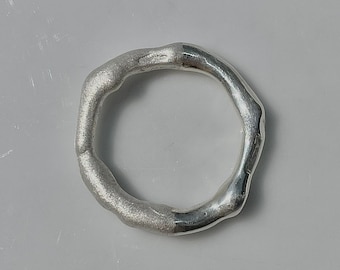 Puede incluir: Un anillo de plata con una forma irregular y texturada.