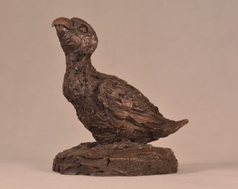 May include: A bronze sculpture of a small bird with its head tilted up, perched on a textured base.