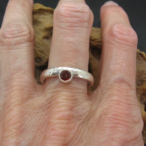 May include: A silver ring with a hammered texture and a small red gemstone set in the centre.