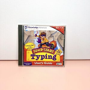May include: A CD-ROM case for "Jump Start Typing" by Knowledge Adventure. The cover features a cartoon character on a keyboard, with the title in large purple letters. The user's guide is also visible. Ages 7-10.