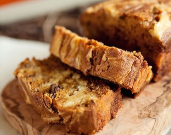May include: Close-up of a loaf of pumpkin bread with swirls of cream cheese frosting. The bread is sliced and arranged on a wooden cutting board.