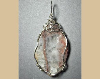 May include: A silver wire wrapped pendant featuring a clear quartz crystal with pink and red inclusions. The pendant is a unique and delicate piece of jewelry.