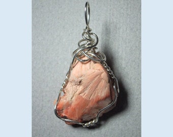 May include: A pink selenite crystal pendant wrapped in silver wire. The crystal has a rough, natural texture and is suspended from a silver bail.