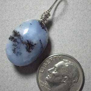 May include: A light blue dendritic opal pendant with a silver wire wrap. The oval-shaped stone features black and brown inclusions. A U.S. dime is next to the pendant for size reference.