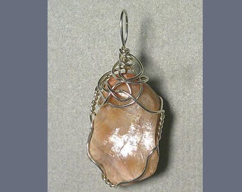 May include: A pendant featuring a peach-colored stone wrapped in silver-colored wire. The wire is intricately woven around the stone, creating a decorative design. The pendant has a loop at the top for hanging.