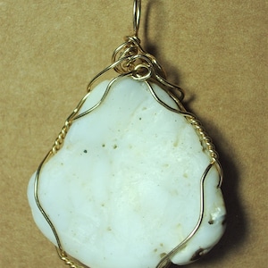 May include: A white, irregularly shaped stone pendant with a gold wire wrap. The wire is twisted and forms a loop at the top for hanging.