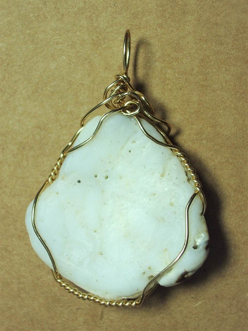 May include: A white, irregularly shaped stone pendant with a gold wire wrap. The wire is twisted and forms a loop at the top for hanging.