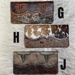 May include: Three rectangular leather wallets labeled G, H, and J. Wallet G features brown embossed steer skulls and cowhide. Wallet H has a brown and white cowhide top with an embossed crocodile texture bottom. Wallet J shows steer skulls and dark fur.