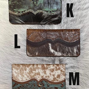 May include: Three rectangular wallets labeled K, L, and M. Wallet K is green with a skull design and black hair-on-hide. Wallet L is brown with floral embossing and brown hair-on-hide. Wallet M is tan hair-on-hide with a teal floral embossed leather.
