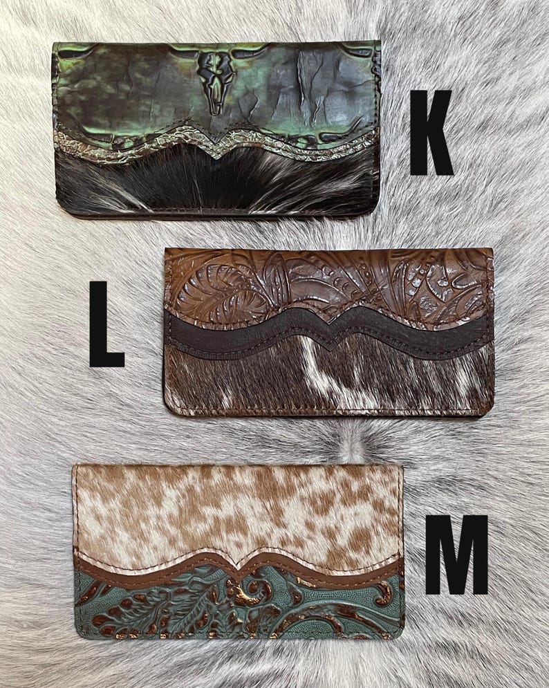 May include: Three rectangular wallets labeled K, L, and M. Wallet K is green with a skull design and black hair-on-hide. Wallet L is brown with floral embossing and brown hair-on-hide. Wallet M is tan hair-on-hide with a teal floral embossed leather.