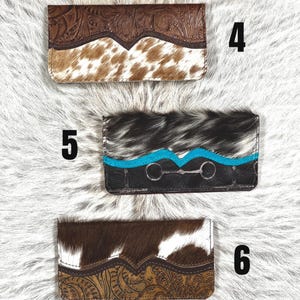May include: Three rectangular wallets labeled 4, 5, and 6. Wallet 4 features brown floral-tooled leather and white and brown cowhide. Wallet 5 has black and white cowhide, a turquoise accent strip, and a silver-toned bit detail. Wallet 6 has brown floral-tooled leather and white and brown cowhide.