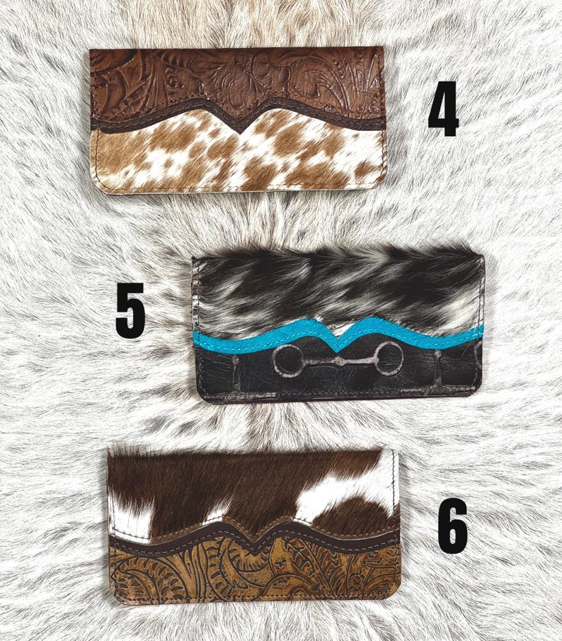 May include: Three rectangular wallets labeled 4, 5, and 6. Wallet 4 features brown floral-tooled leather and white and brown cowhide. Wallet 5 has black and white cowhide, a turquoise accent strip, and a silver-toned bit detail. Wallet 6 has brown floral-tooled leather and white and brown cowhide.