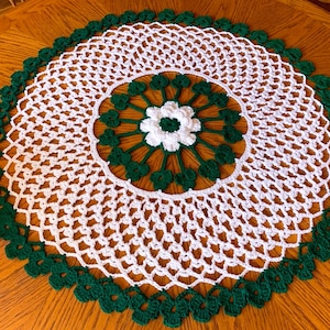 May include: White crochet table runner with a green crocheted border and a white flower in the centre.