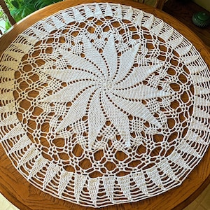May include: White crocheted table runner with a circular design featuring a swirling pattern in the center.
