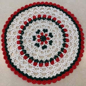 May include: A white crocheted doily with a green and red border. The doily has a circular design with a central flower motif.