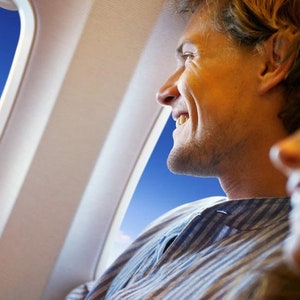 May include: A man and a woman are sitting next to each other on an airplane, looking out the window. The man is smiling and the woman is laughing.