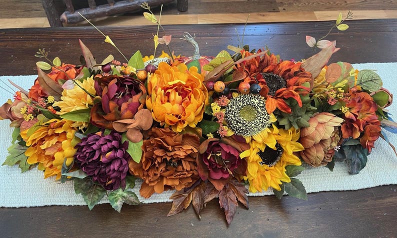 Puede incluir: Un centro de mesa de tem&aacute;tica oto&ntilde;al con una mezcla de flores naranja, amarillo, burdeos y marr&oacute;n. El centro de mesa incluye girasoles, peon&iacute;as y otras flores oto&ntilde;ales.