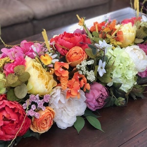Puede incluir: Un arreglo floral colorido con flores rosas, blancas, amarillas, naranjas y rojas. El arreglo es perfecto para una pieza central o decoración de mesa.