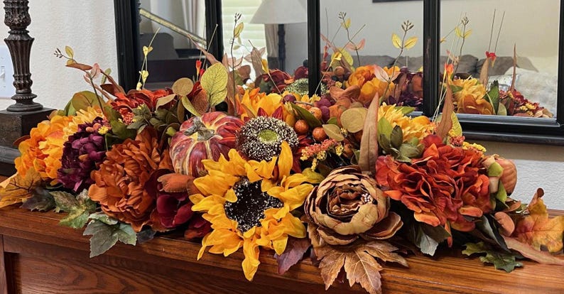 Puede incluir: Un centro de mesa de oto&ntilde;o con girasoles, peon&iacute;as burdeos y naranja, una peque&ntilde;a calabaza y follaje oto&ntilde;al.