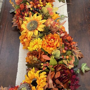 Puede incluir: Un camino de mesa de oto&ntilde;o con girasoles, flores naranja y burdeos y hojas verdes.
