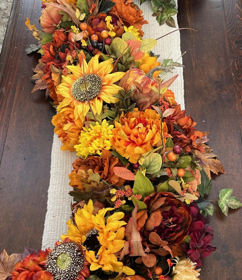 Puede incluir: Un camino de mesa de oto&ntilde;o con girasoles, flores naranja y burdeos y hojas verdes.