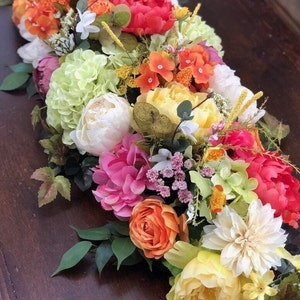 May include: A colorful floral arrangement with a variety of flowers, including peonies, hydrangeas, roses, and dahlias. The arrangement is in shades of pink, orange, yellow, and white.