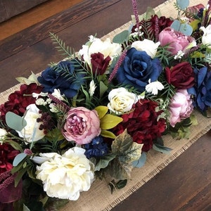 Puede incluir: Un centro de mesa floral largo, de color burdeos, blanco y azul con vegetación y un camino de mesa de arpillera. El centro de mesa está hecho de flores de seda y es perfecto para una boda o un evento especial.