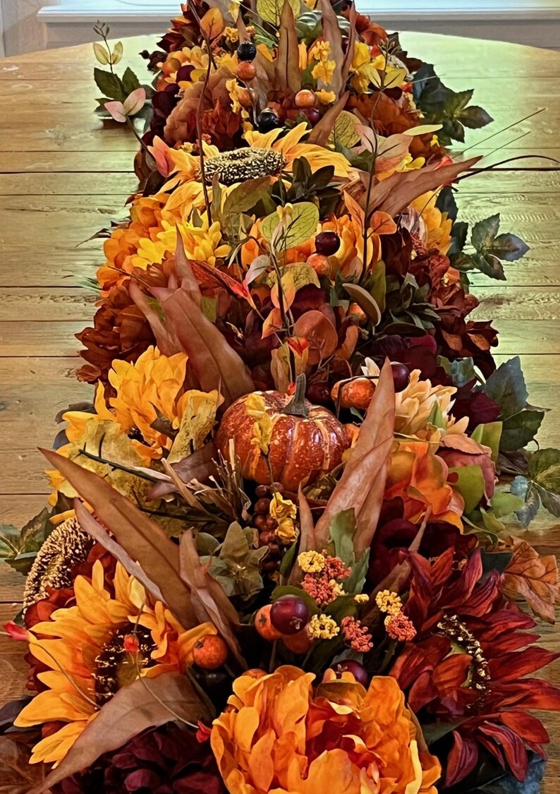 Puede incluir: Un camino de mesa de oto&ntilde;o con girasoles, calabazas, bayas y hojas en tonos naranja, rojo y marr&oacute;n.