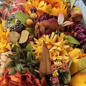 Puede incluir: Un arreglo floral de tem&aacute;tica oto&ntilde;al con una variedad de flores en tonos naranja, amarillo, rojo y marr&oacute;n. El arreglo incluye girasoles, crisantemos y otras hojas de oto&ntilde;o.