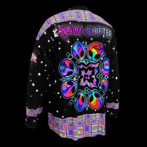 Könnte beinhalten: Schwarzes Langarmshirt mit einem lebendigen, farbenfrohen Alien-Design und dem Text "REALM SHIFTER". Das Shirt hat ein geometrisches Muster am Kragen und Saum, mit weißen Stern- und Punktakzenten.